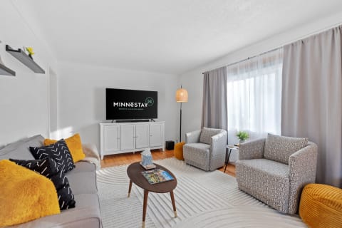 A cozy living room with a gray sofa, two geometric armchairs, and a wall-mounted TV.