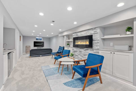 Modern basement living room featuring blue chairs, a fireplace, and a television.
