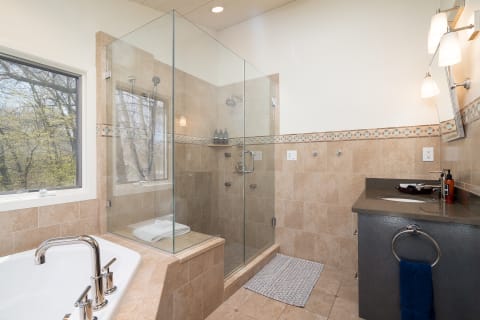 Modern bathroom featuring a glass shower, bathtub, and natural light from a window.