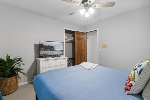 Cozy bedroom with a blue bed, decorative pillow, and a TV displaying coastal scenery.