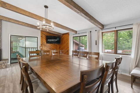 Dining room featuring a large wooden table, high-backed chairs, rustic beams, and a TV.