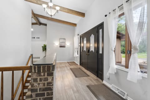 A spacious entryway with a chandelier, wooden beams, and double doors.