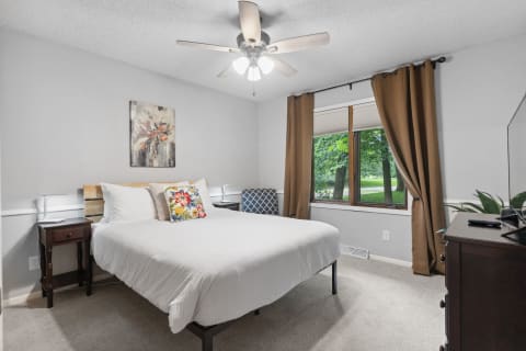 A cozy bedroom with a bed, decorative pillow, nightstand, and window view.