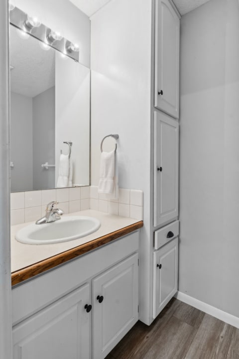 Compact bathroom with a white sink and wooden countertop, illuminated by five light fixtures.
