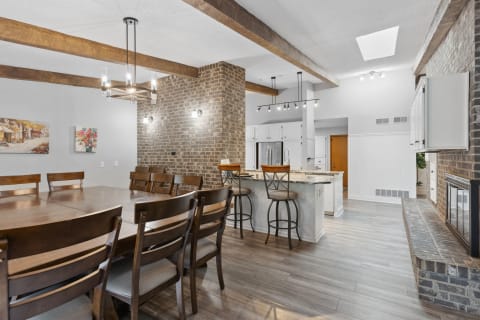 View of a modern dining room and kitchen with wooden beams and brick walls.