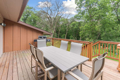 Spacious wooden deck with a gray dining table and grill, set in a natural outdoor environment.