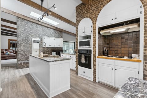 Contemporary kitchen with granite island, white cabinetry, and exposed brick.