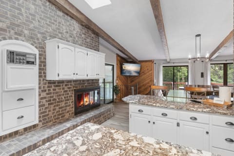 Modern kitchen with white cabinets, brick fireplace, and a wooden dining area.