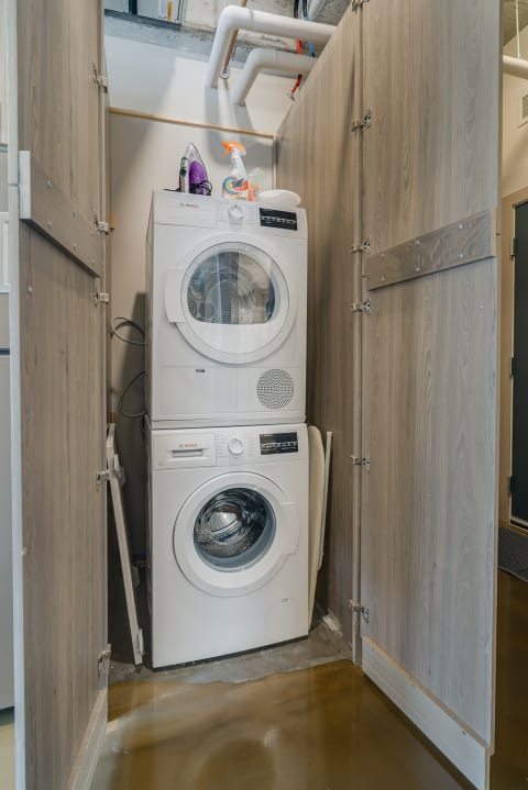 Stacked white washer and dryer in a compact wooden enclosure, with household items on top.