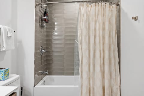 A contemporary bathroom showcasing a shower with a patterned curtain, gray tiles, and organized toiletries.