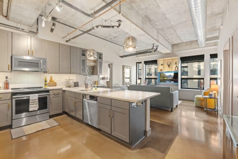 Modern kitchen with gray cabinets and a cozy living area visible in the background.