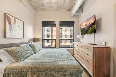 Modern bedroom with a cozy bed, abstract art, and large windows.