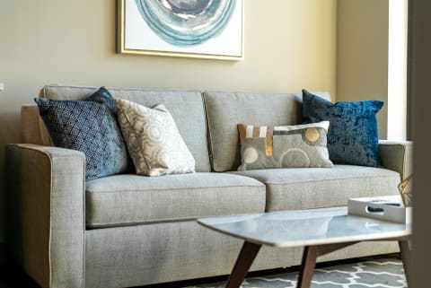 Modern gray sofa with decorative pillows and a marble coffee table in a bright living room.