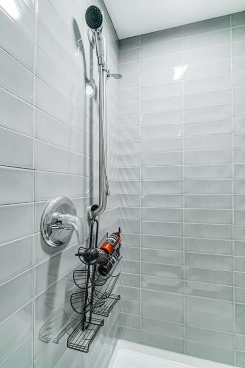 Contemporary shower with chrome showerhead, faucet, and a wire shelf holding shampoo bottles.