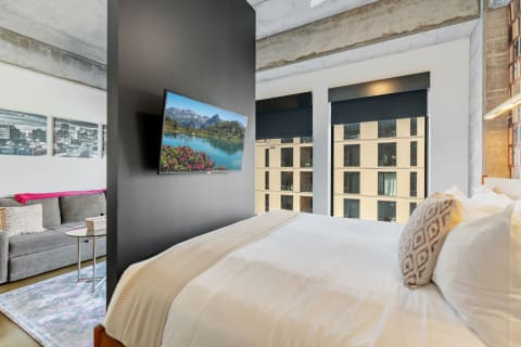 Stylish bedroom featuring a bed, sofa, and flat-screen TV with a scenic picture.