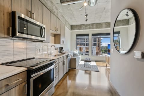 A contemporary kitchen and living room in an apartment featuring wooden cabinets, stainless steel appliances, and large windows.