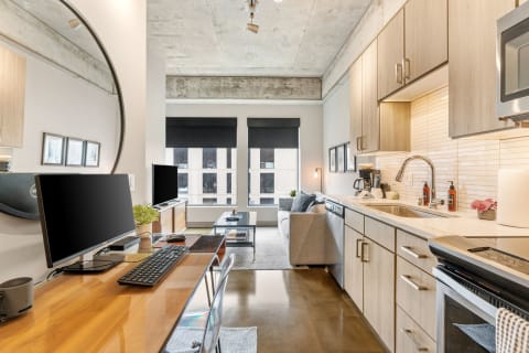 A stylish apartment with a kitchen and living area, featuring modern decor and an industrial ceiling.