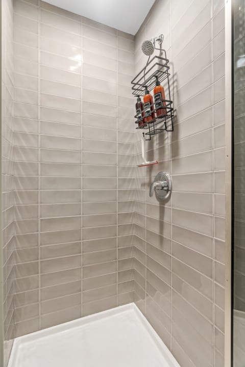 Modern shower enclosure with light beige tiles and black metal caddy holding shampoo bottles.