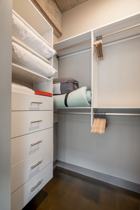 Interior view of a modern closet with shelves and drawers, displaying bedding and hangers.