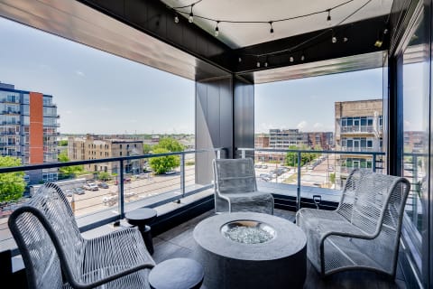 A modern balcony featuring wicker chairs and a stone fire pit with city views.