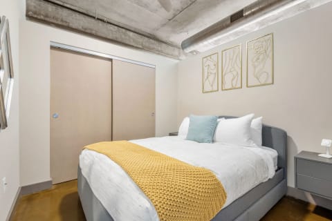 Contemporary bedroom with a queen bed, yellow knitted throw, and line-art decorations.