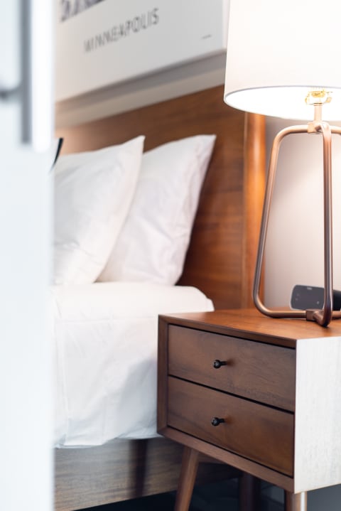 A bedside table with a lamp and an artworks in a beautifully arranged bedroom.