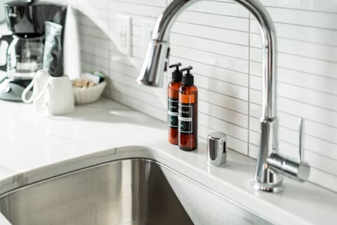 Modern kitchen sink with stainless steel sink, chrome faucet, amber soap bottles, and a coffee maker in the background.