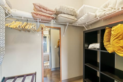 Neatly organized closet featuring shelves with pillows, hangers, a mirror, and a black shelving unit.
