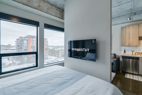 A contemporary bedroom with a view of snow-covered buildings outside the window and a TV on the wall.