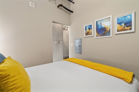 Cozy bedroom with a white bed, yellow blanket, and decorative framed artwork.