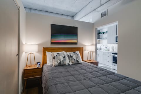 Cozy bedroom featuring a queen bed, decorative pillows, and an adjoining kitchenette.