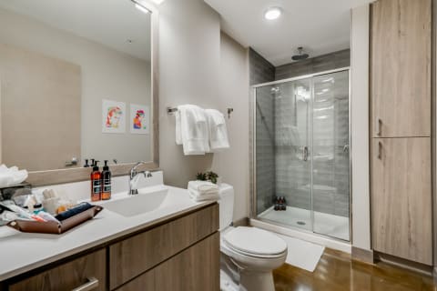 A contemporary bathroom featuring a glass shower, vanity with toiletries, and colorful wall art.