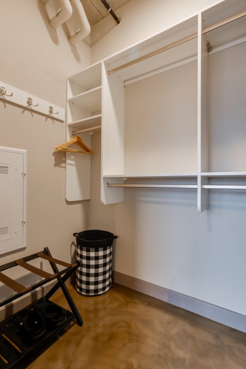 Minimalistic closet with white shelves, wooden hanger, and a checkered laundry basket.