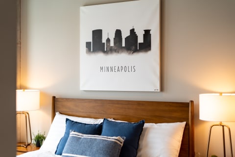 Cozy bedroom with Minneapolis skyline artwork and blue pillows on a wooden bed.