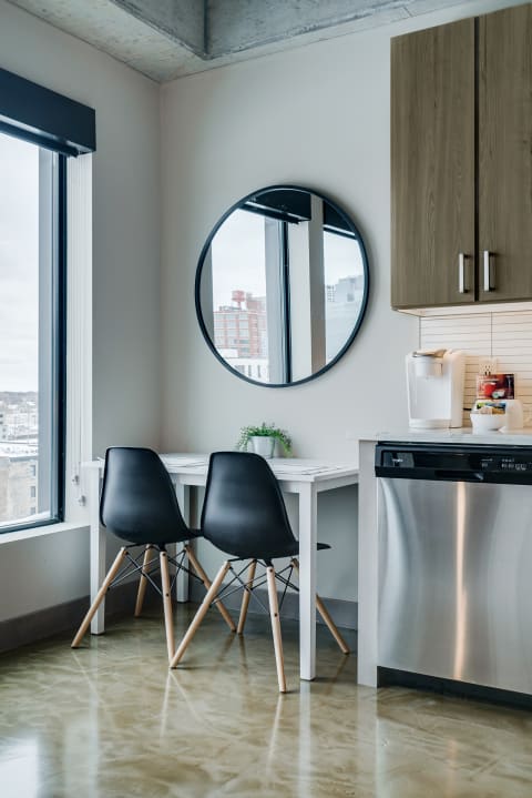 Modern dining area with a white table, black chairs, and a large round mirror.