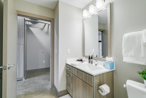 A contemporary bathroom with a wooden vanity, white countertop, and concrete floor.