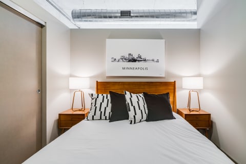 Modern bedroom interior with a bed, patterned pillows, nightstands, and skyline art of Minneapolis.