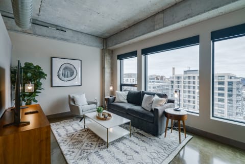 Modern living room with a gray sofa, armchair, and large windows overlooking an urban landscape.