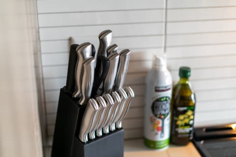 A knife block with stainless steel knives, cooking spray, and olive oil on a kitchen countertop.