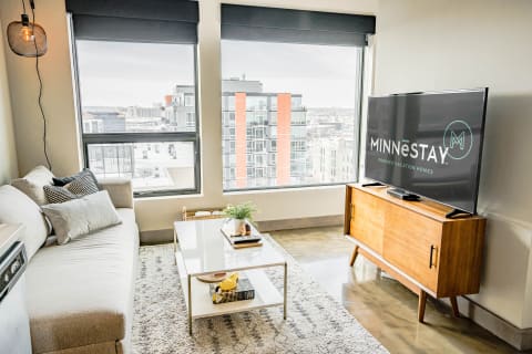 Stylish living room with a city view, featuring a gray couch and a wooden TV stand.