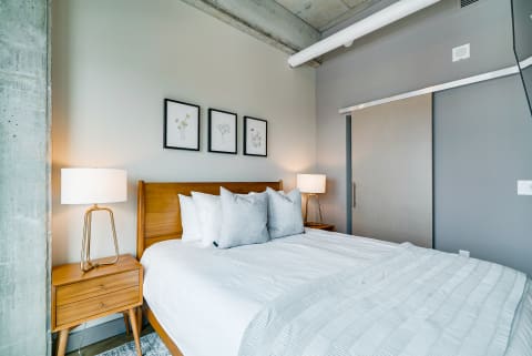 Modern bedroom with a wooden bed, grey throw pillows, and framed botanical prints.