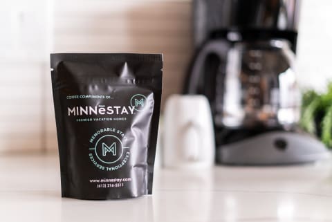 A packet of coffee labeled MINNESTAY in a contemporary kitchen, with a coffee maker and creamer in view.