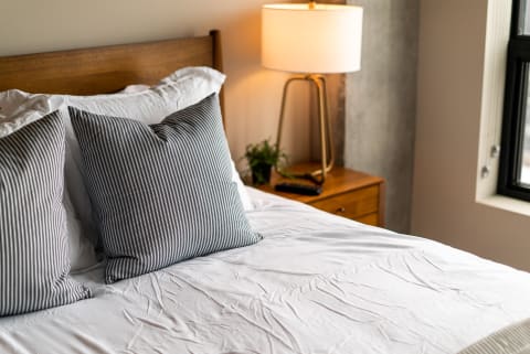 A neatly arranged bed with striped pillows, a bedside table, and a lamp.