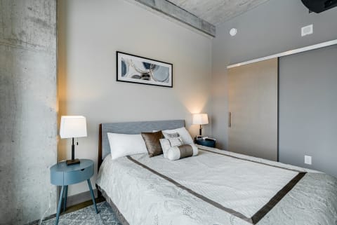 A contemporary bedroom featuring a neatly made bed, beside lamps, and modern artwork.