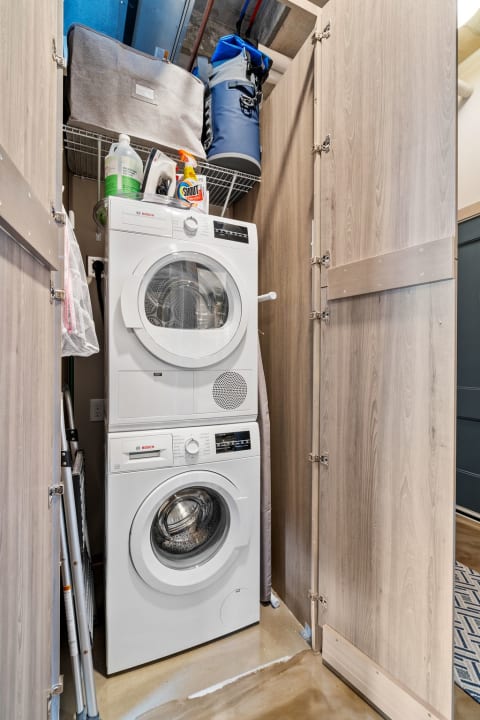 A compact laundry area with a stacked Bosch washer and dryer surrounded by wooden cabinetry and shelving.