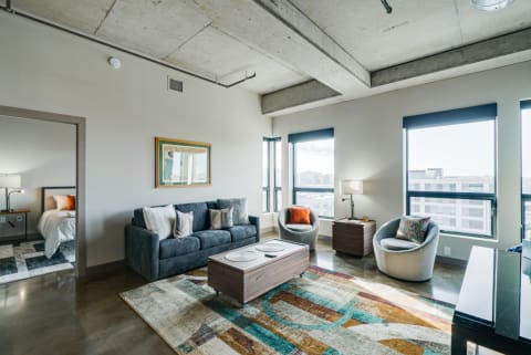 Modern living room with gray sofa, armchairs, and large windows showcasing a city view.
