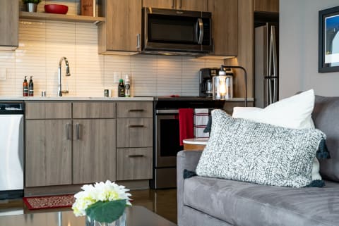 A modern kitchen with gray cabinets and a cozy living area with decorative pillows and flowers.