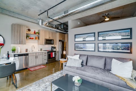 Open-concept apartment featuring a modern kitchen and living area with gray couch and cityscape art.
