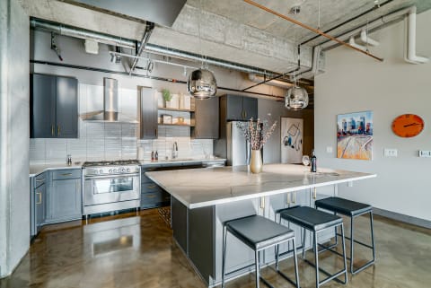 Modern kitchen featuring grey cabinets, marble countertop, and chrome pendant lights.