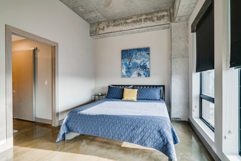 A cozy bedroom with a blue bedspread and colorful wall art.